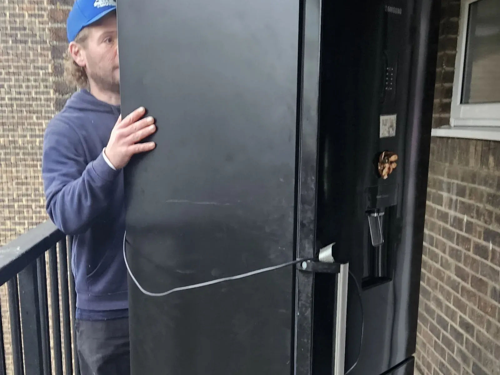 MV Movers crew member steadying a large fridge freezer on an outside stairwell during an appliance removal in West London