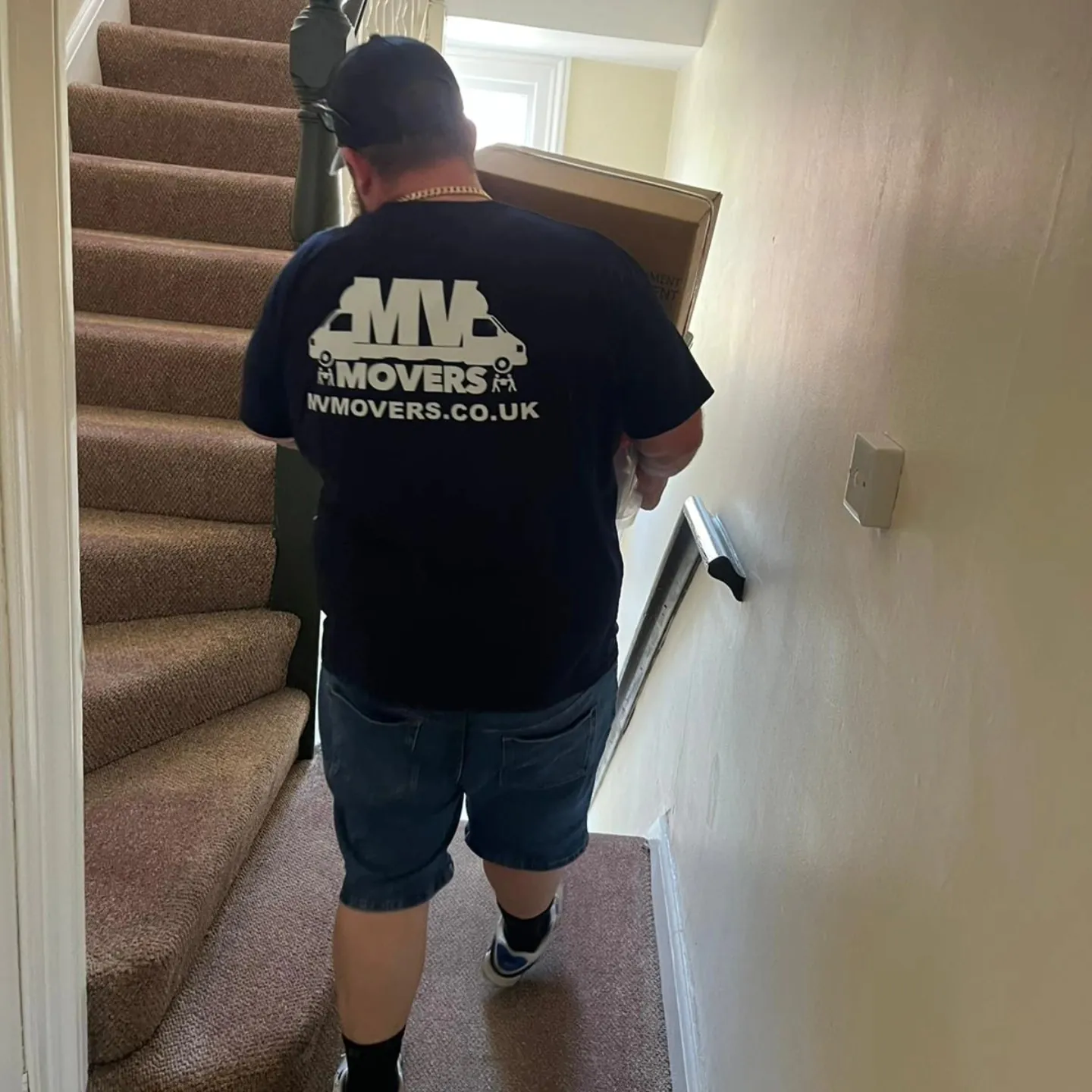 MV Movers crew carrying furniture up a narrow staircase in a West London house